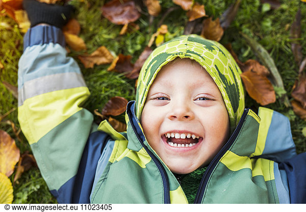 Portrait of cheerful boy lying on ground in forest during autumn