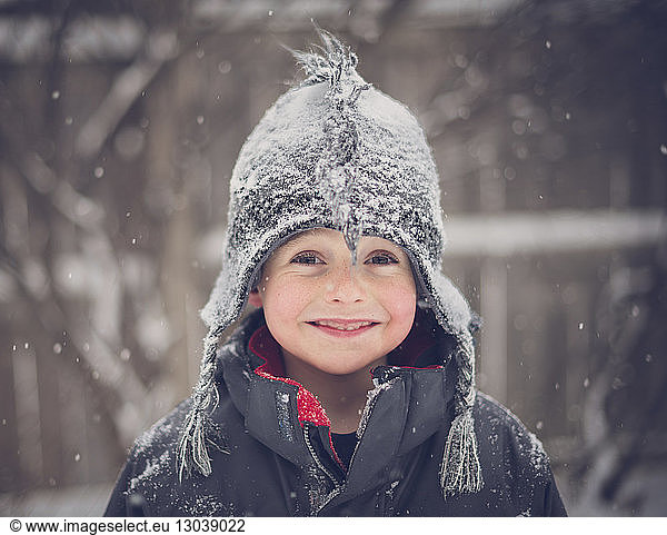 Portrait of cheerful boy wearing hat during snowfall