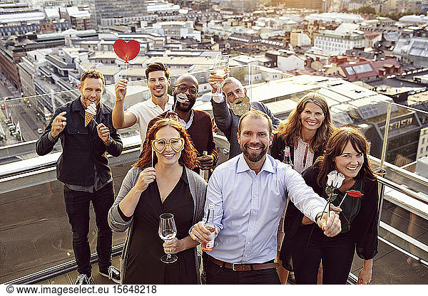 Portrait of cheerful business team with props and drinks enjoying after work party on terrace