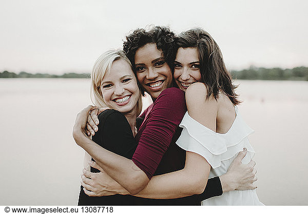 Portrait of cheerful female friends embracing against lake
