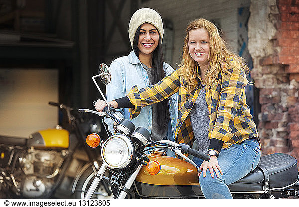 Portrait of cheerful female friends with bike outside auto repair shop