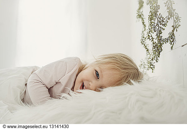 Portrait of cheerful girl lying on fur blanket at home