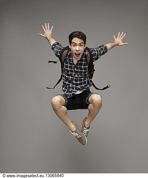 Portrait of cheerful man with backpack jumping against gray background