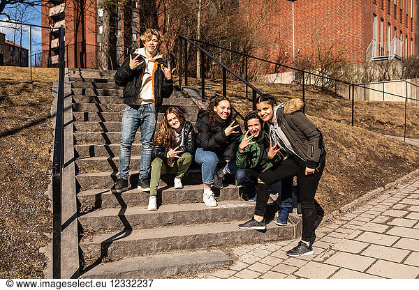 Portrait of cheerful multi-ethnic teenage friends showing hand signs on steps in city