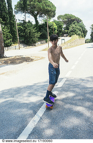 Portrait of cheerful shirtless teen skateboarding on mountain road