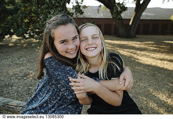 Portrait of cheerful sisters embracing at farm