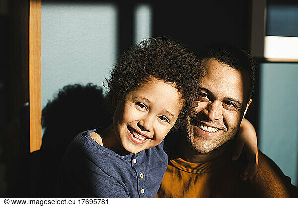 Portrait of cheerful son with arm around father during sunny day at home