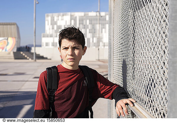Portrait of cheerful teen leaning on metallic fence while looking away