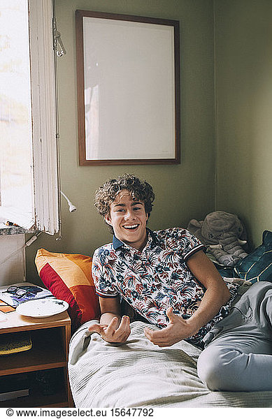 Portrait of cheerful teenage boy leaning on bed at home