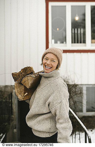 Portrait of cheerful woman carrying firewood during winter