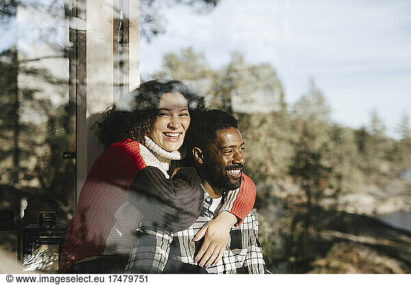 Portrait of cheerful woman embracing boyfriend seen through window