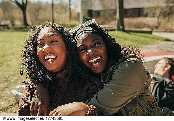 Portrait of cheerful woman embracing female friend in playground on sunny day
