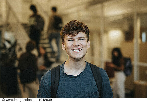 Portrait of cheerful young male student standing in university