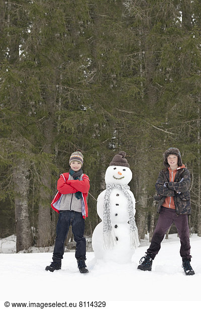 Portrait of confident boys next to snowman in woods