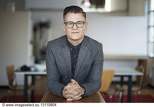 Portrait of confident businessman leaning on wooden table at office