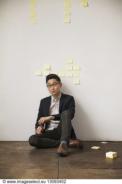 Portrait of confident businessman sitting against wall in creative office