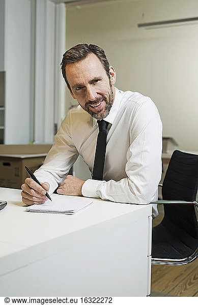 Portrait of confident businessman sitting at desk in office taking notes