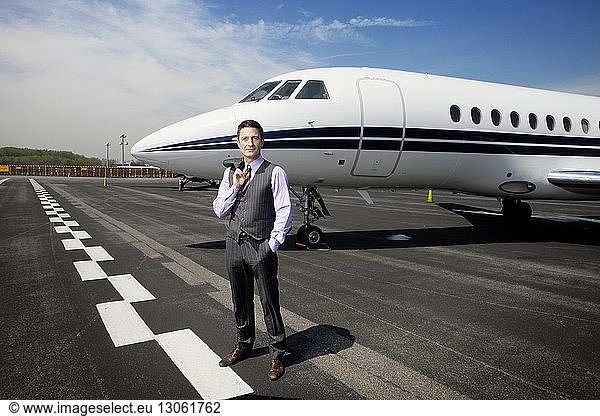 Portrait of confident businessman standing against corporate jet on runway