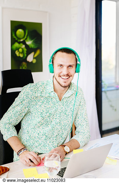 Portrait of confident businessman wearing headphones at office desk