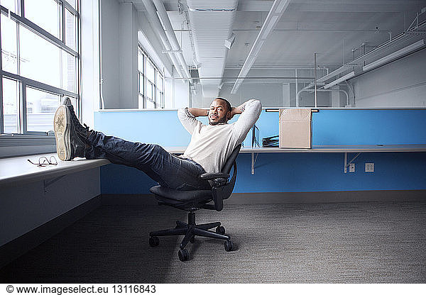 Portrait of confident businessman with hands behind head sitting on chair in office