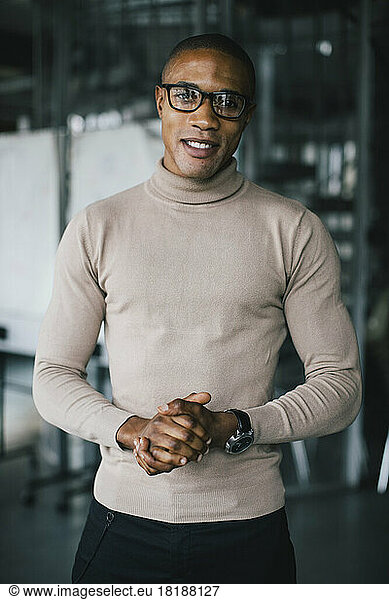 Portrait of confident businessman with hands clasped standing in office
