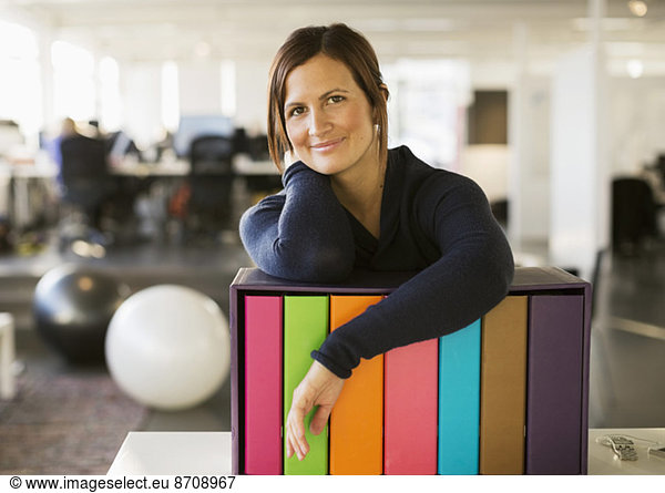Portrait of confident businesswoman leaning on folder rack in office