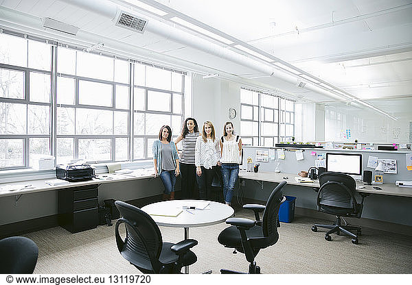 Portrait of confident businesswomen standing by desk in office