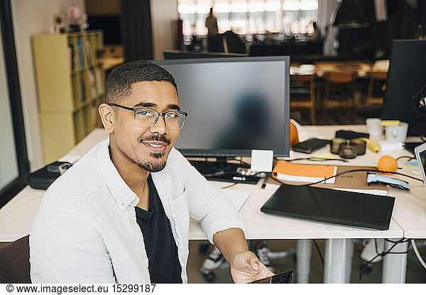 Portrait of confident computer hacker sitting at desk in office