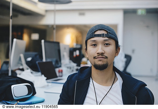 Portrait of confident computer programmer wearing cap in office
