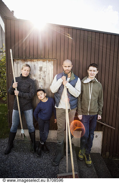 Portrait of confident family with gardening equipment standing against house