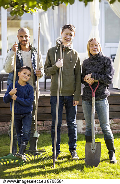 Portrait of confident family with gardening equipment standing at yard