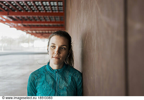 Portrait of confident female athlete leaning against brick wall