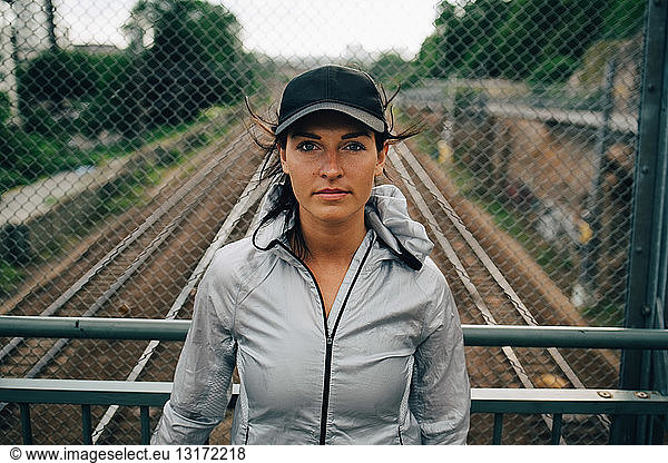 Portrait of confident female athlete standing against railing on bridge