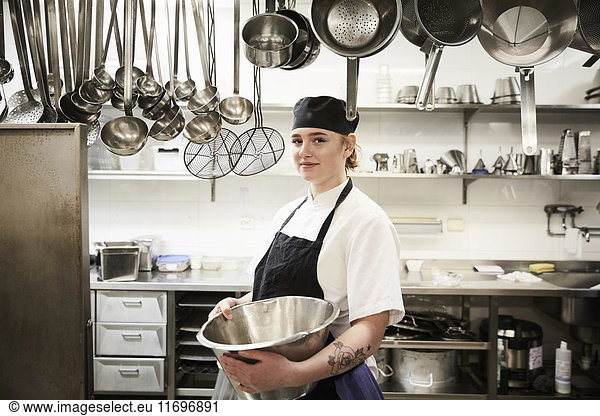Portrait of confident female chef holding container in commercial kitchen