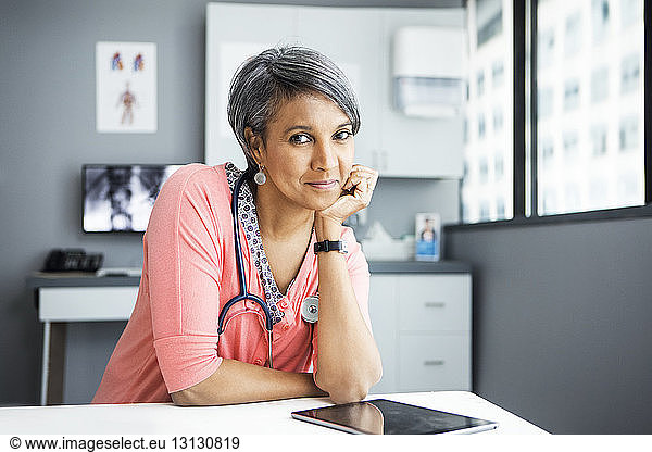 Portrait of confident female doctor leaning on desk in clinic