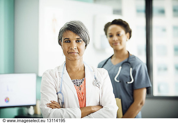 Portrait of confident female doctor standing arms crossed with colleague in background