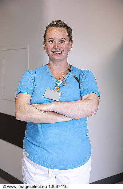 Portrait of confident female doctor with arms crossed standing against wall in hospital corridor