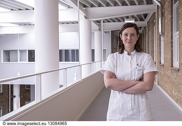 Portrait of confident female doctor with arms crossed standing in hospital corridor