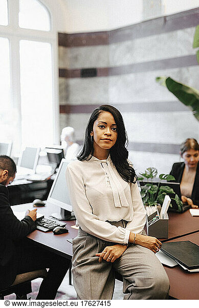 Portrait of confident female financial advisor sitting on desk in law office