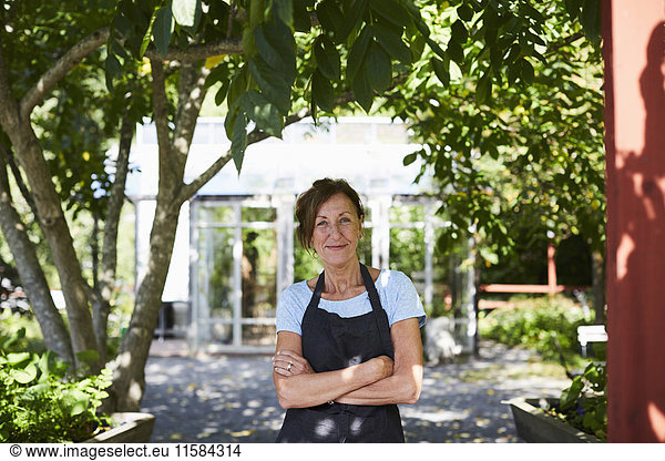 Portrait of confident female gardener standing arms crossed at yard