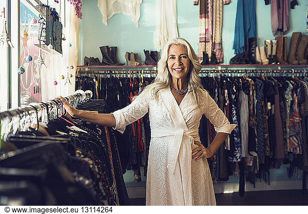 Portrait of confident female owner smiling by clothing rack in store