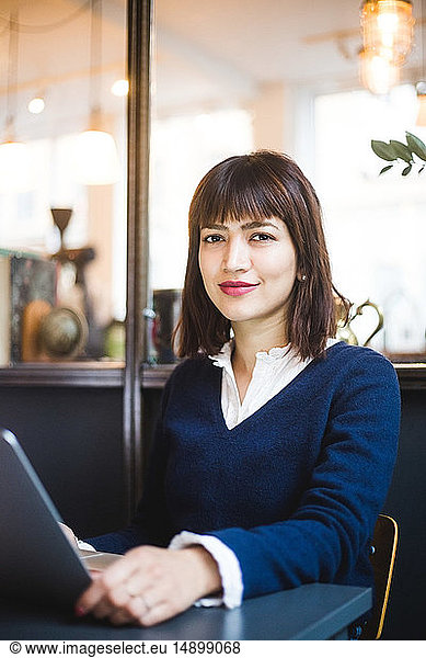 Portrait of confident female professional sitting with laptop at office