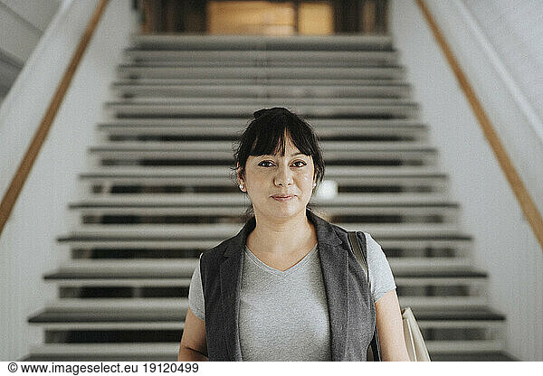 Portrait of confident female professor standing against steps in university