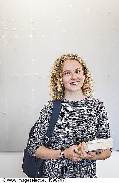 Portrait of confident female student standing against wall in university