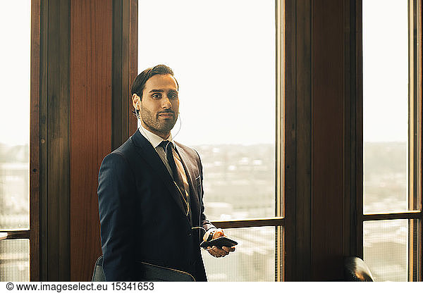 Portrait of confident financial advisor with smart phone against window at law office