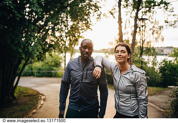 Portrait of confident male and female athletes standing on road in park