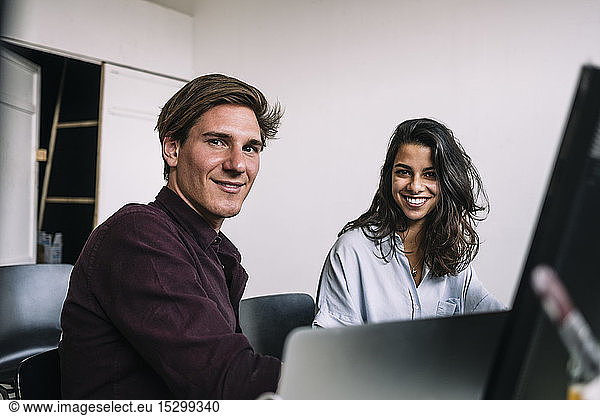 Portrait of confident male and female IT professionals sitting at desk in creative office
