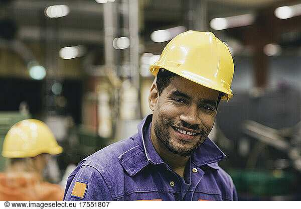 Portrait of confident male blue-collar worker wearing hardhat in factory
