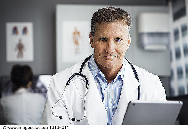 Portrait of confident male doctor holding tablet computer in clinic