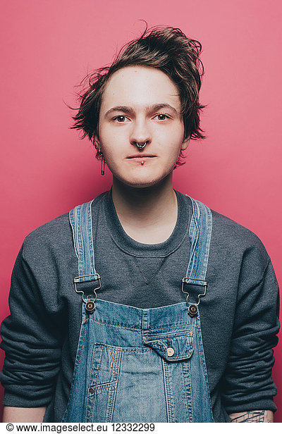 Portrait of confident male hipster wearing overalls over pink background